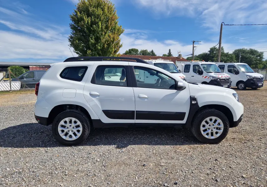 Vue de profil côté gauche d'un Dacia Duster blanc 4x4 2023 avec barres de toit et jantes alliage 16 pouces.