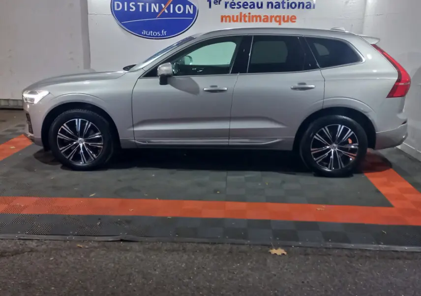 Profil côté gauche d'un Volvo XC60 gris clair 2022 garé en intérieur avec jantes alliage et feux arrière LED visibles.