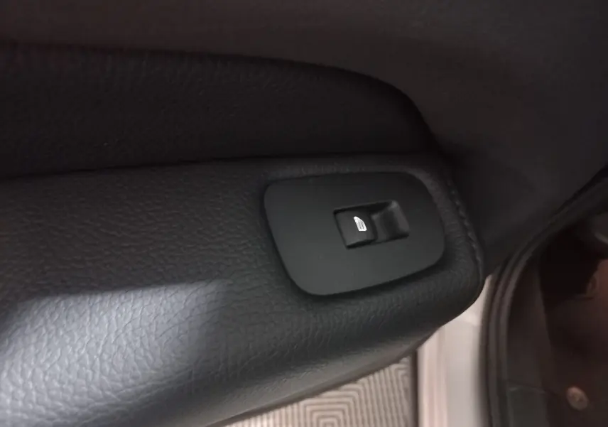 Gros plan sur le bouton de commande de lève-vitre arrière droit en plastique noir dans un Volvo XC60 gris clair 2022.