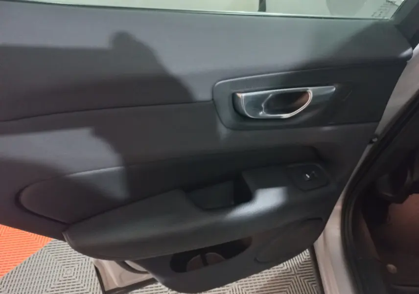 Gros plan sur la porte intérieure côté gauche du Volvo XC60 gris clair, avec poignée métal et commande de fenêtre.