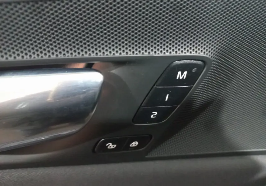 Gros plan sur la poignée de porte intérieure et les boutons de mémoire des sièges du Volvo XC60 gris clair 2022.