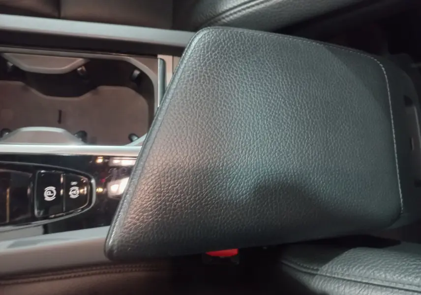 Gros plan sur l'accoudoir central en cuir noir et la console avec commandes électroniques du Volvo XC60 gris clair.