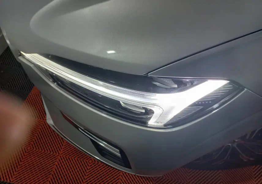 Gros plan sur le phare avant droit allumé d’un Volvo XC60 gris clair, soulignant son design LED distinctif.