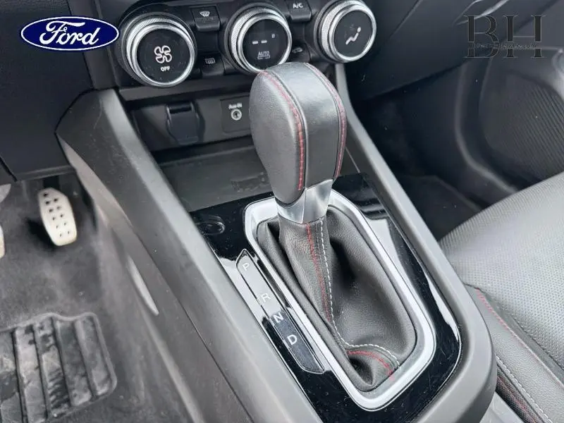 Gros plan sur la console centrale et levier de vitesses automatique en cuir noir avec surpiqûres rouges, intérieur gris.