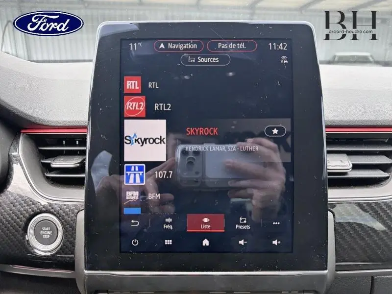 Tableau de bord avec écran tactile central affichant les radios, entouré de finitions carbone et bouton Start/Stop visible à gauche.