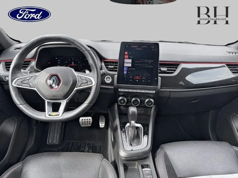 Vue intérieure avant du tableau de bord et volant cuir noir du Renault Arkana gris métallisé, avec écran tactile vertical et levier de boîte auto.