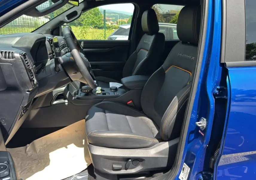 Vue intérieure côté conducteur du Ford Ranger Wildtrak X 2026 bleu lightning, sièges noirs avec surpiqûres orange et volant cuir multifonctions.