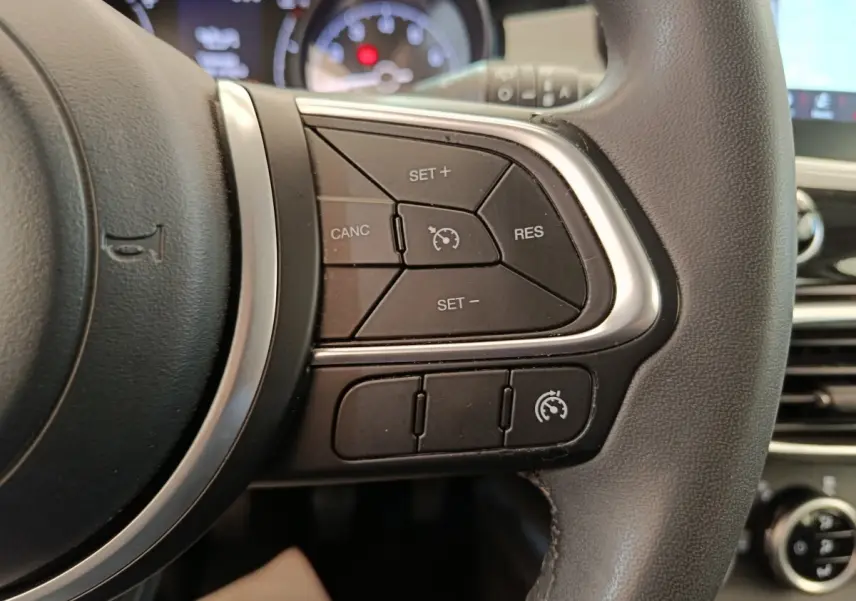 Gros plan sur les commandes du régulateur de vitesse au volant cuir noir de la FIAT 500X blanche, tableau de bord en arrière-plan flou.