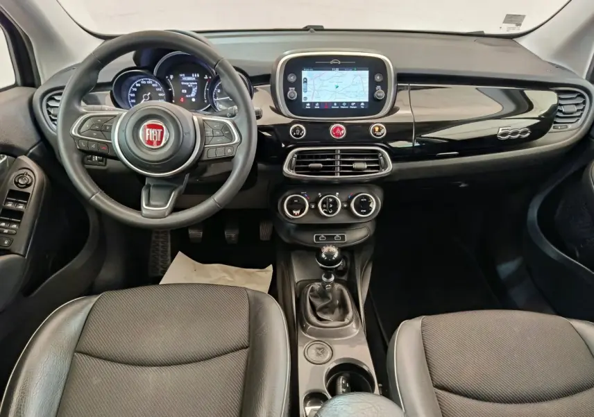 Vue intérieure avant du tableau de bord noir brillant et volant cuir de la Fiat 500X 2020 avec écran tactile et boîte manuelle.