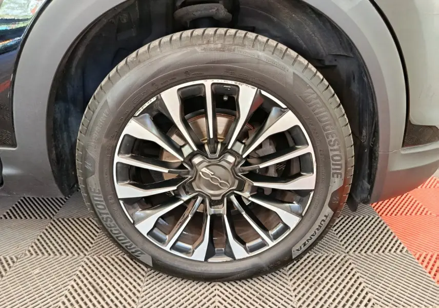 Gros plan sur la roue avant droite avec jante alliage noire et argentée du FIAT 500X blanc.