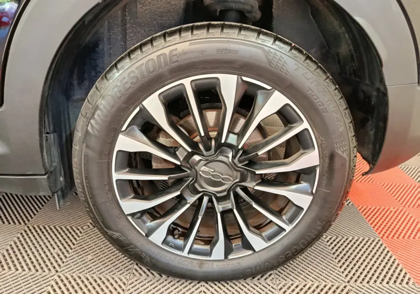 Gros plan sur la roue avant droite de la Fiat 500X blanche, avec jante alliage noire et argentée distinctive.