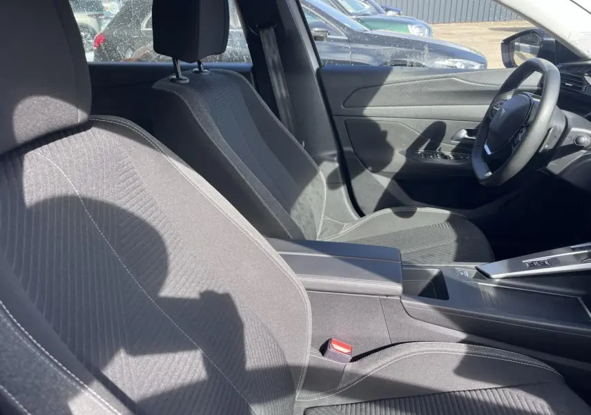 Intérieur avant de la Peugeot 308 2024, vue côté droit sur sièges tissu gris et console centrale avec accoudoir.