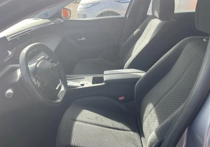 Vue intérieure côté conducteur de la Peugeot 308 2024, sièges tissu gris et volant multifonction noir.