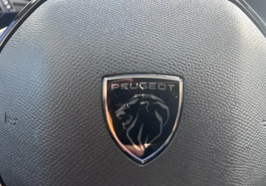 Gros plan sur le volant noir texturé avec logo Peugeot en relief au centre, intérieur de la Peugeot 308 2024.