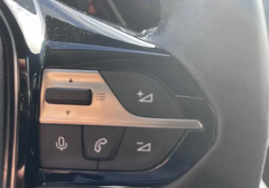 Gros plan sur les commandes multifonctions au volant noir de la Peugeot 308 2024, version essence gris Artense.