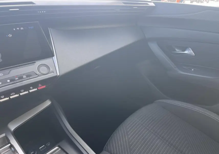 Vue intérieure côté passager de la Peugeot 308 2024 avec siège tissu noir et tableau de bord moderne.