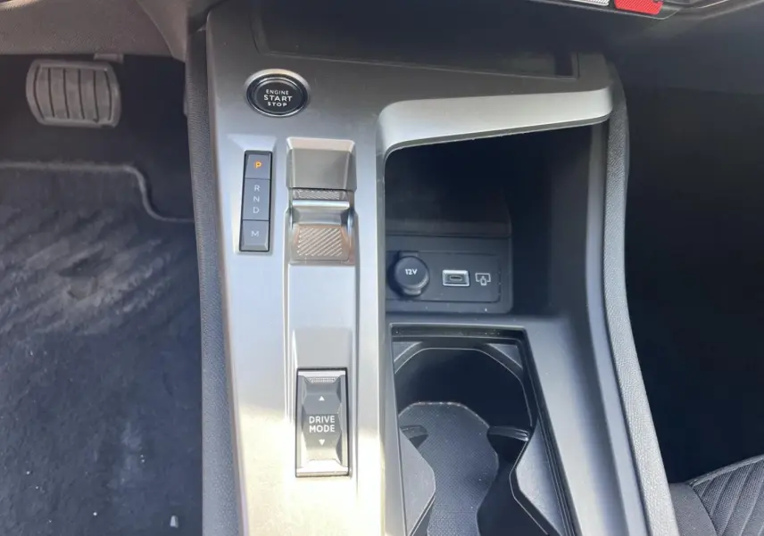 Vue rapprochée de la console centrale grise de la Peugeot 308 2024 avec sélecteur de boîte auto et prise 12V visible.