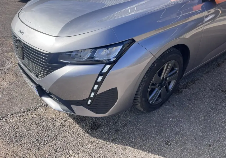 Vue 3/4 avant droit d'une Peugeot 308 gris Artense avec phares LED et calandre noire distinctive.