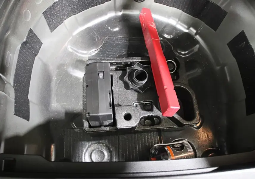 Coffre ouvert montrant le rangement sous plancher avec kit de réparation pneus et triangle de signalisation rouge.