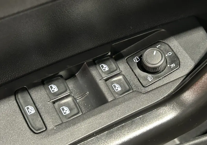 Gros plan sur les commandes de lève-vitres et réglage des rétroviseurs côté conducteur d’une Volkswagen Polo noire.