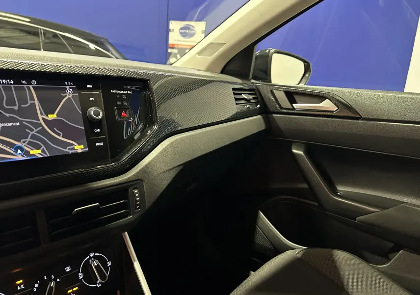 Vue intérieure côté passager du tableau de bord noir de la Volkswagen Polo 2022 avec écran GPS et finitions modernes.