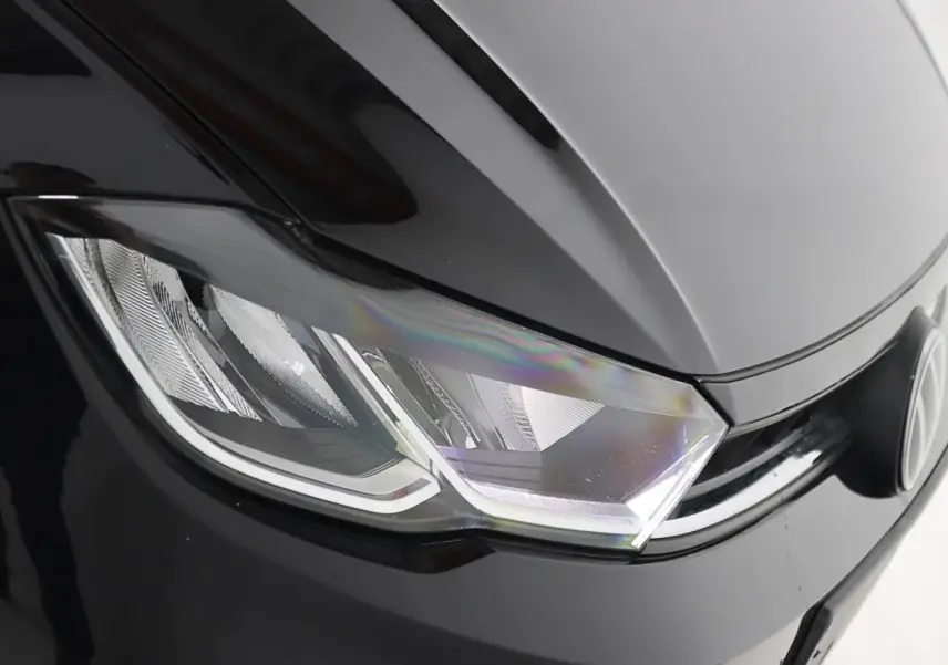 Gros plan sur le phare avant gauche noir brillant d'une Volkswagen Polo 2022 avec logo VW visible.