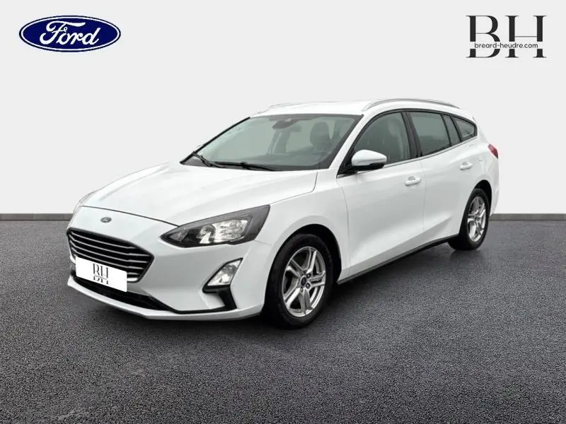 Ford Focus SW blanc glacier vue 3/4 avant droit avec jantes alu et barres de toit visibles.