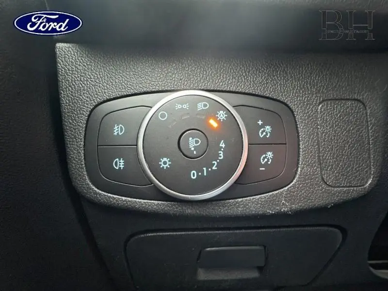 Gros plan sur le bouton de réglage des phares d’un Ford Focus SW blanc Glacier, avec témoin lumineux orange allumé.