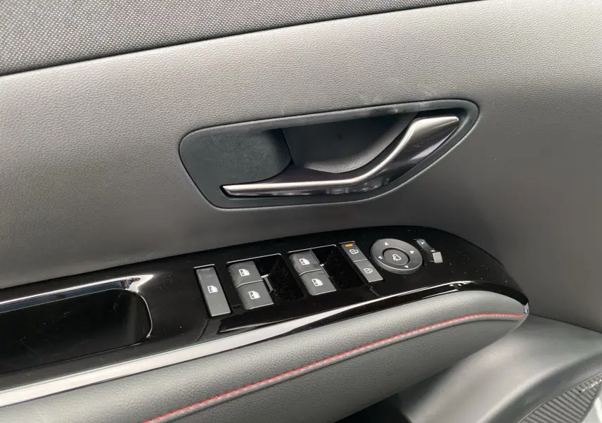 Gros plan sur la poignée intérieure et les commandes de vitres côté gauche du Hyundai Tucson gris avec surpiqûres rouges.