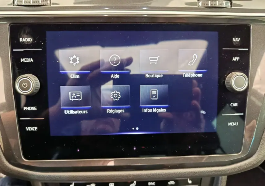 Écran tactile central du Volkswagen Tiguan 1.4 eHybrid 2023 affichant le menu principal avec options clim, aide, boutique et téléphone.