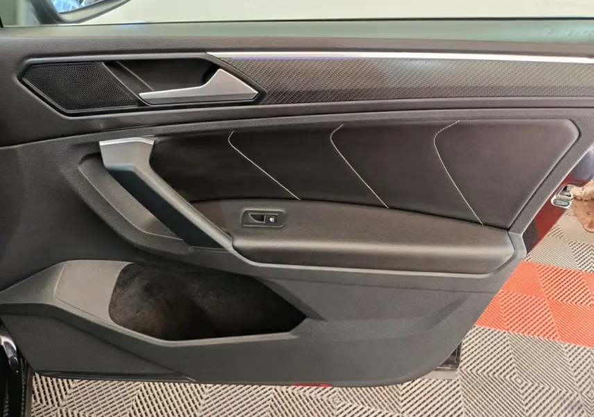 Gros plan sur la porte intérieure côté gauche du Volkswagen Tiguan noir, avec surpiqûres et poignée argentée.