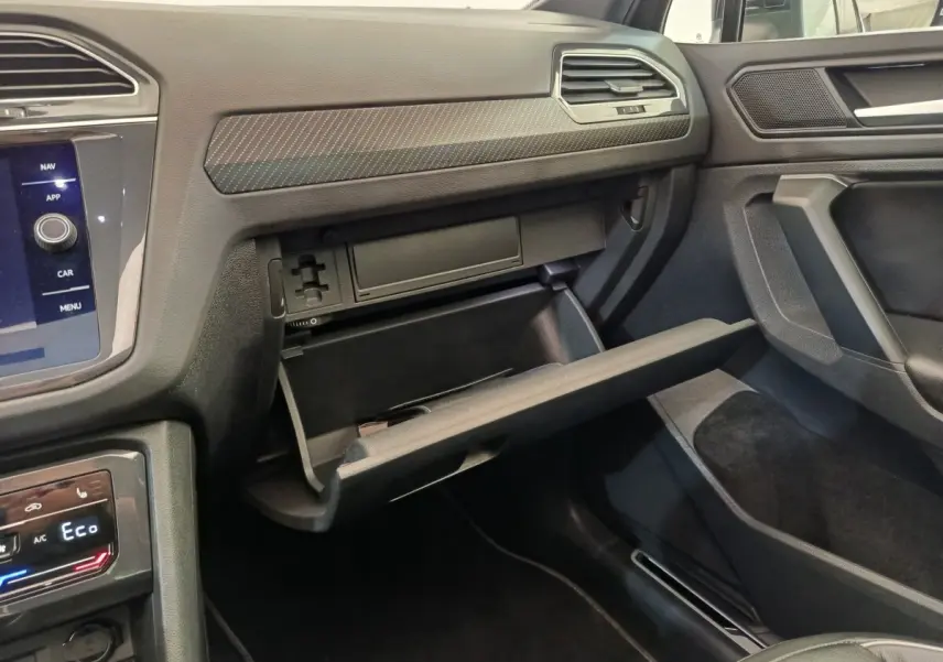 Intérieur du Volkswagen Tiguan 2023, vue côté passager sur la boîte à gants ouverte et tableau de bord noir.