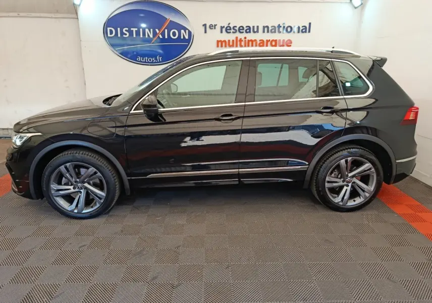 Vue de profil côté gauche du Volkswagen Tiguan noir 1.4 eHybrid 245 DSG6 R-Line Exclusive 2023 en intérieur showroom.