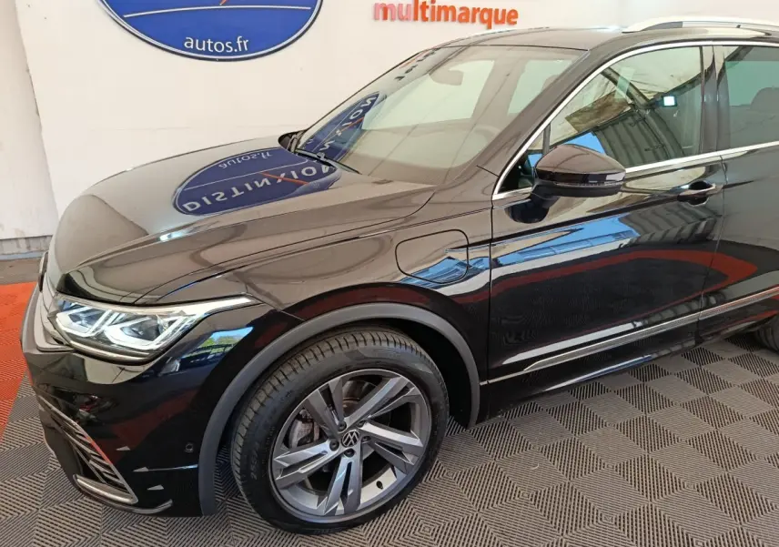 Vue de trois quarts avant droit du Volkswagen Tiguan noir 1.4 eHybrid avec jantes alliage et prise de recharge latérale.