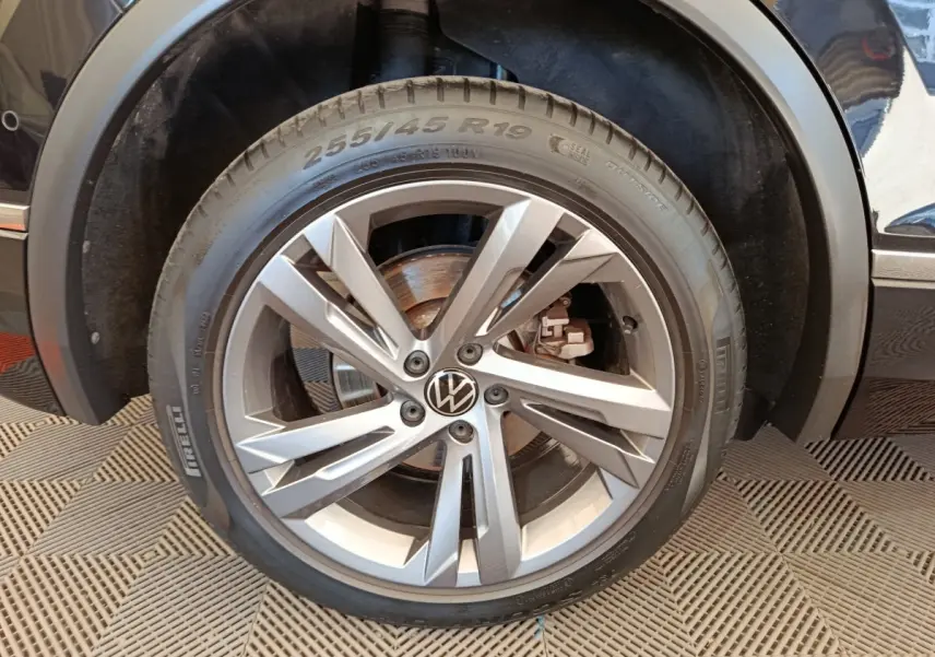 Gros plan sur la roue avant droite du Volkswagen Tiguan noir, mettant en valeur la jante alliage et le logo VW central.