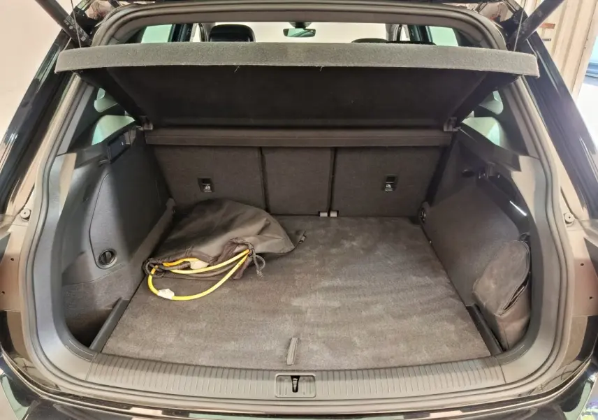 Coffre ouvert d’un Volkswagen Tiguan noir 2023, vue arrière, avec câble de recharge et cache-bagages déployé.