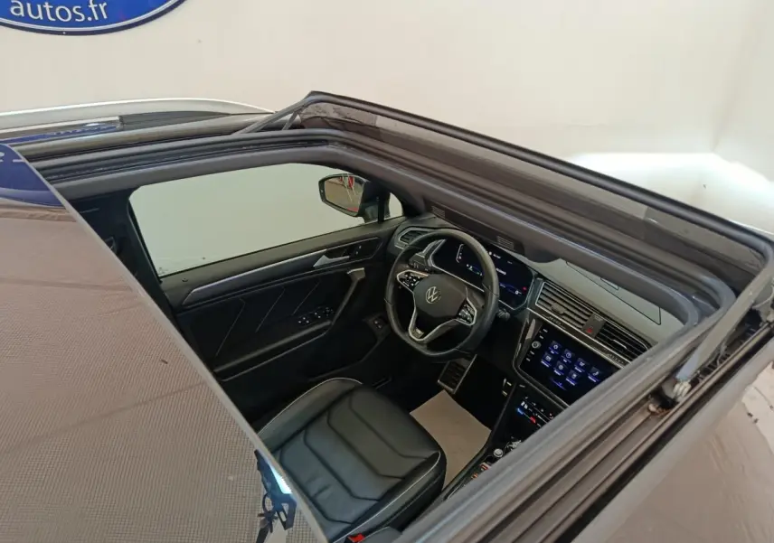 Vue intérieure par le toit ouvrant du Volkswagen Tiguan noir, mettant en valeur le volant cuir et l'écran tactile central.