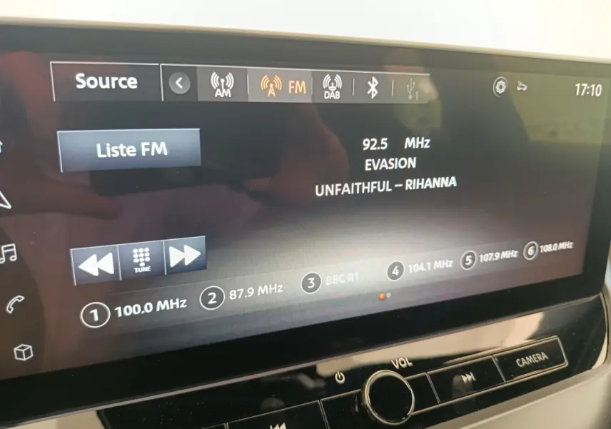 Écran tactile central du Nissan Juke bleu 2025 affichant la radio FM avec station et titre de chanson visibles.