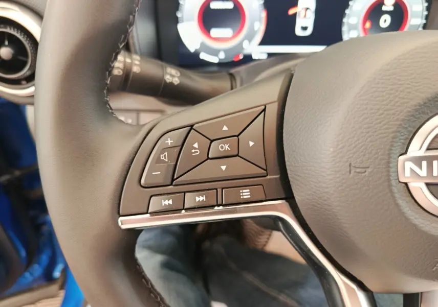 Gros plan sur les commandes gauche du volant cuir du Nissan Juke bleu, avec affichage numérique en arrière-plan.