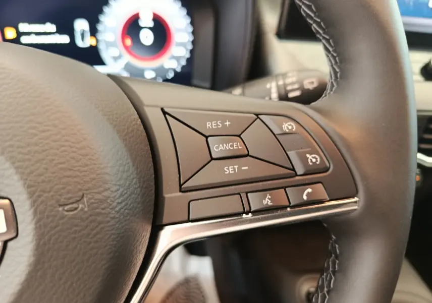 Gros plan sur les commandes multifonctions du volant cuir noir du Nissan Juke bleu 2025, avec tableau de bord numérique en arrière-plan.