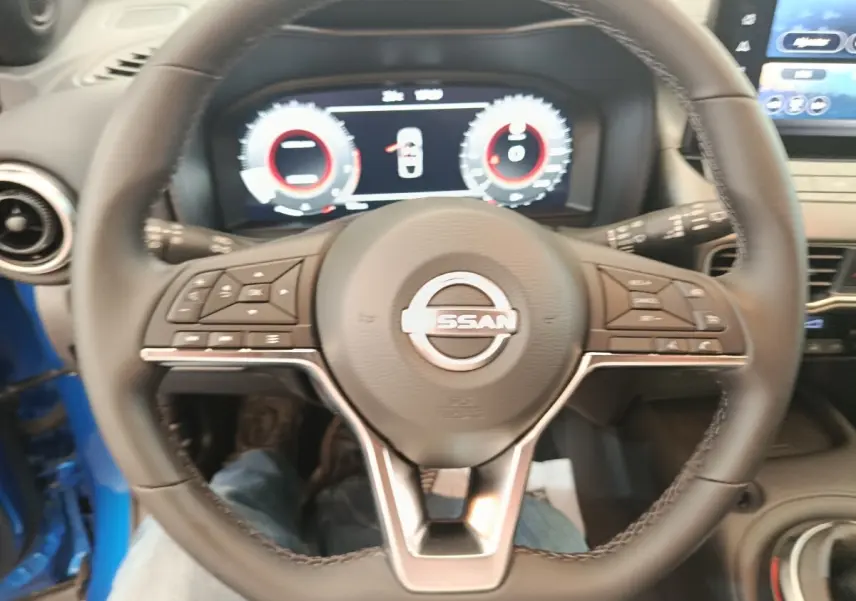 Vue rapprochée du volant cuir noir du Nissan Juke bleu 2025 avec tableau de bord numérique et écran tactile central.