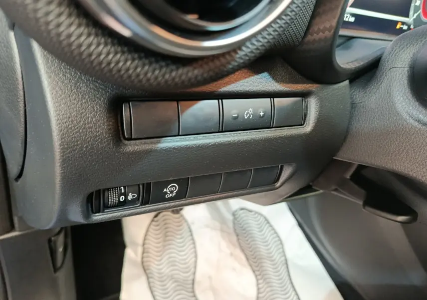 Détail des commandes d’éclairage et réglages au tableau de bord côté gauche du Nissan Juke bleu 2025.