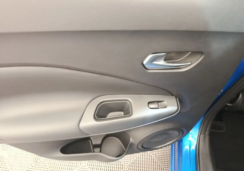 Intérieur côté droit de la porte avant d’un Nissan Juke bleu 2025 avec poignée argentée et haut-parleur intégré.