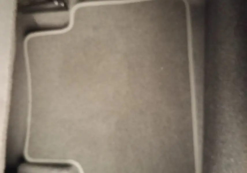 Vue rapprochée du tapis de sol gris foncé à bordures claires dans l'habitacle du Nissan Juke bleu 2025.