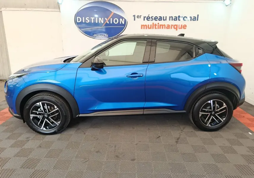 Vue de profil côté gauche d'un Nissan Juke bleu 2025 avec toit noir et jantes alliage bicolores.