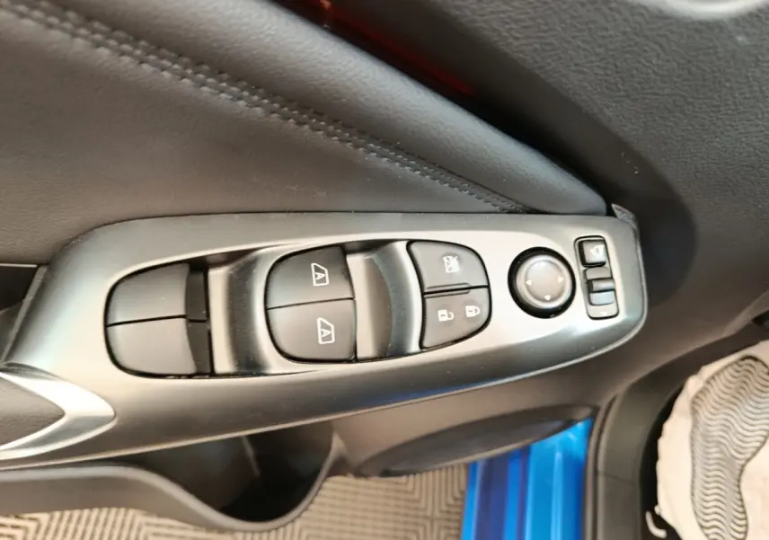Gros plan sur les commandes des vitres et rétroviseurs côté conducteur du Nissan Juke bleu 2025, intérieur noir.