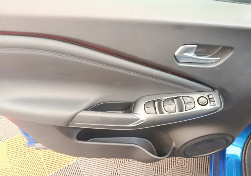 Vue intérieure côté gauche de la porte avant d’un Nissan Juke bleu avec commandes de vitres et poignée argentée.