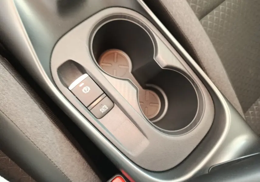 Gros plan sur la console centrale noire du Nissan Juke bleu 2025, avec porte-gobelets et frein à main électrique.