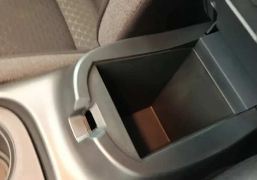 Vue rapprochée de l'accoudoir central avant ouvert du Nissan Juke bleu, montrant le rangement intérieur vide.