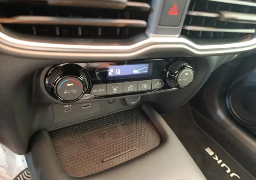 Détail de la console centrale du Nissan Juke bleu 2025, montrant les commandes de climatisation et un espace de recharge sans fil.